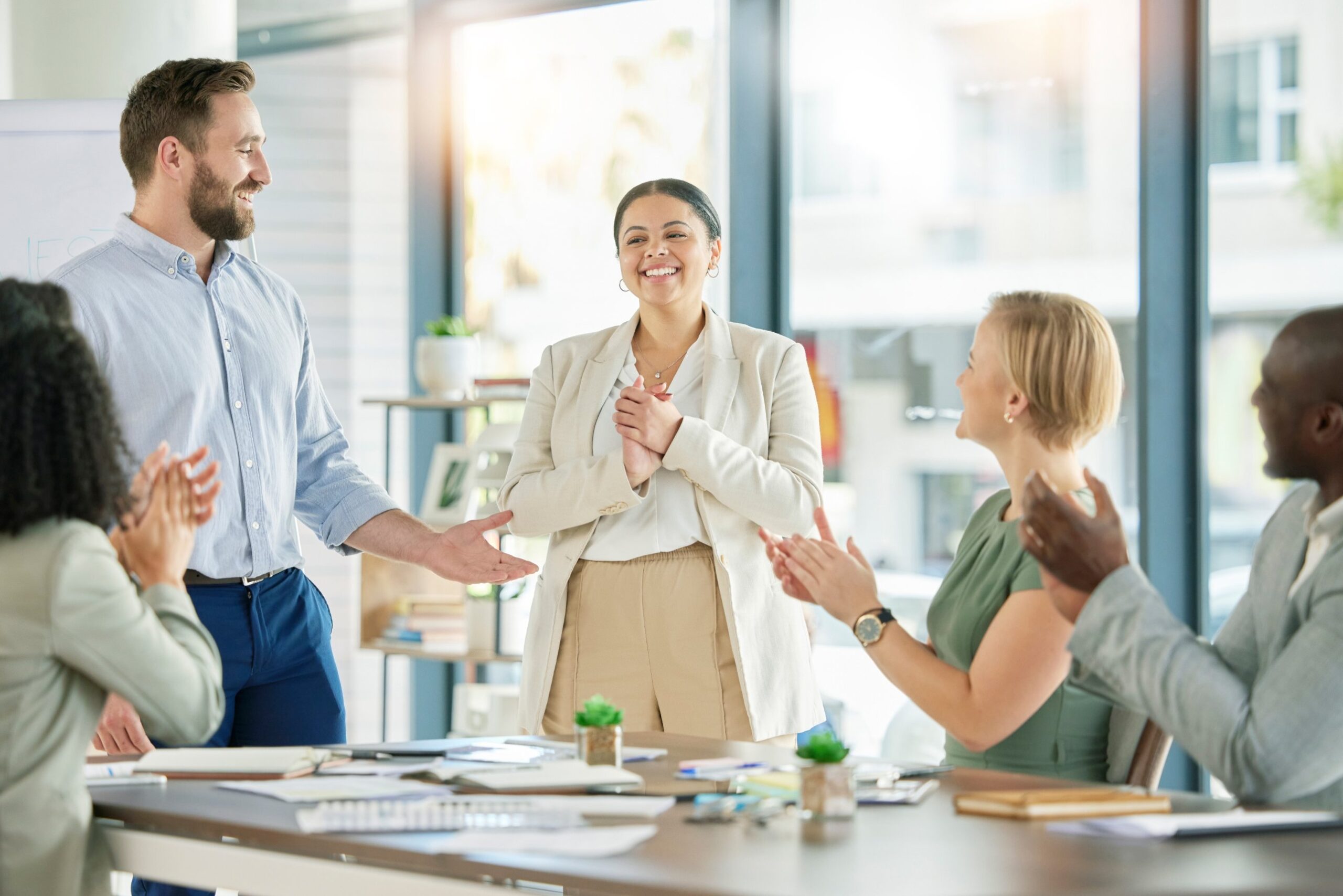 Coworkers applauding a smiling colleague in a meeting room as her promotion is announced