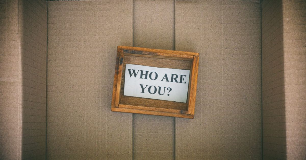 A small wooden frame reading "Who are you?" inside an empty cardboard box